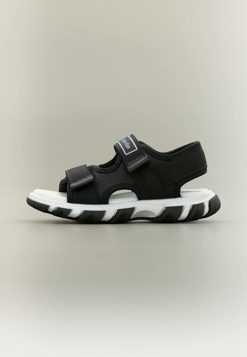 Αθλητικό σανδάλι ασπρόμαυρο με ρυθμιζόμενα λουράκια και παχύ πέλμα, σχεδιασμένο για άνεση και καθημερινή χρήση.