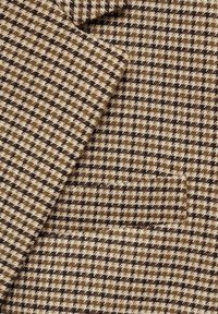 Tissu à motif pied-de-poule marron, beige et noir plié, montrant la texture et le détail de la poche tissée.