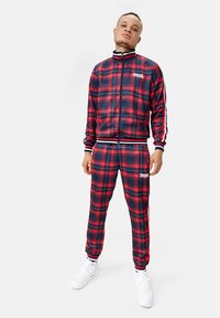Red and navy plaid tracksuit with a zip-up jacket and elastic waist pants; white accents; made from smooth, lightweight fabric.
