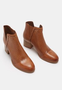 Brązowe botki ze skóry z ażurowym wzorem, szpiczastym noskiem i obcasem na słupku. Posiadają elastyczne panele boczne ułatwiające zakładanie.