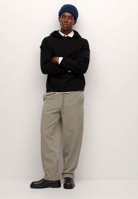 Fekete kapucnis pulóver, világos khaki nadrág és fekete cipők. A modell kék kötött sapkát és fehér galléros inget visel a kapucnis pulóver alatt.