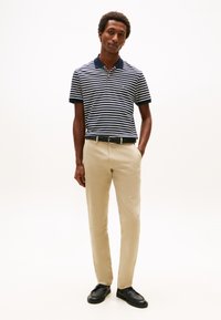 Csíkos póló sötétkék és fehér színben, bézs nadrág, fekete öv és cipők. Simogató tapintású anyag; rövid ujjú, kontrasztos gallérral és mandzsettával.