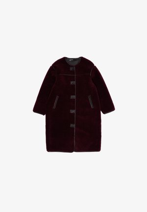 Burgundowy, pluszowy płaszcz z okrągłym dekoltem, czarnymi akcentami, pięcioma guzikami z przodu i bocznymi kieszeniami. Długie rękawy i luźny krój.