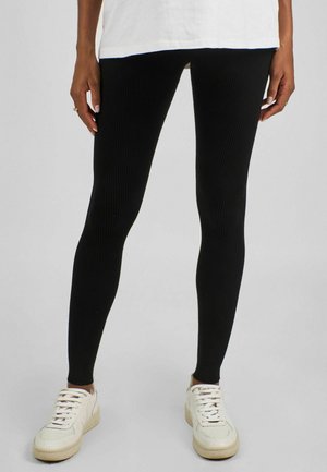 Schwarze Ripp leggings mit enger Passform, kombiniert mit weißen Sneakers, die ein schlichtes und glattes Design ohne zusätzliche Muster oder Akzente aufweisen.
