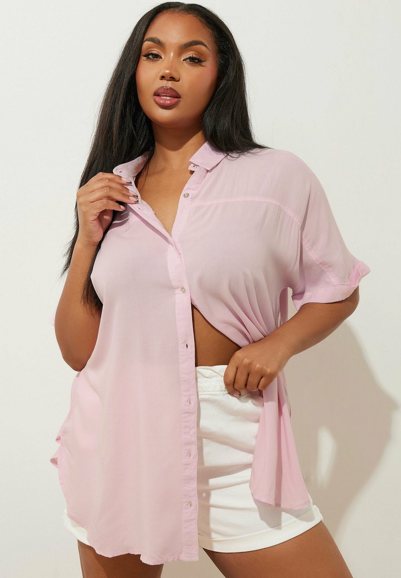 Ljusrosa, skjorta med knappar och korta ärmar i en avslappnad passform. Bärs öppen, vilket visar vita shorts under. Mjuk, lätt tygtextur.