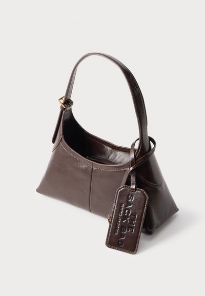 Sac à main en cuir marron foncé avec une seule bandoulière et une étiquette embossée avec "THE SOCK BAG."