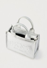 Väike metallik hõbedane DKNY New York käekott kahe käepidemega ja osaliselt avatud tõmblukuga peal.