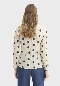 Blouse crème clair avec de grands pois bleu marine, manches longues et texture froissée. Poignets boutonnés et ourlet arrondi.