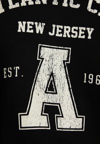 Tela negra con una gran letra "A" blanca desgastada, con "ATLANTIC CITY" y "NEW JERSEY" impresos en una fuente envejecida.