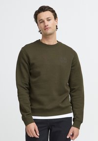 Olijfgroene sweatshirt met een ronde halslijn, lange mouwen en geribde manchetten. Heeft een subtiele tekstontwerp op de borst. Zacht textuur van de stof.