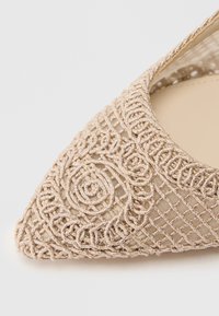 Δείκτης σε στυλ φλατ με περίπλοκη μπεζ κεντητική, διαθέτοντας υφή στην επιφάνεια και λεπτά σχέδια που τονίζουν ένα υoveμένο σχέδιο.