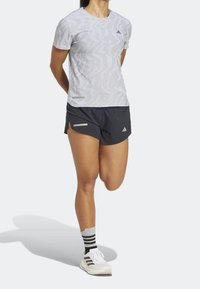 Camiseta atlética de color gris claro con estampado, pantalones cortos negros con aberturas laterales, combinados con zapatos blancos y calcetines a rayas. Acentos reflectantes en los pantalones cortos.