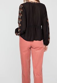 Black blouse with embroidered floral patterns along the sleeves, featuring a gathered waist and a round neckline, paired with light pink pants.