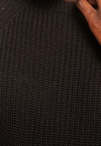 Pull noir en maille présentant un motif texturé avec un col rond. Un gros plan révèle des coutures détaillées et des fibres légèrement en relief.