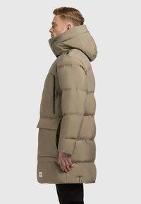 Parka khaki imbottito con colletto alto, tasca laterale con zip e cappuccio regolabile. Realizzato in un materiale liscio e resistente all'acqua.
