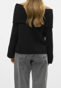 Pull noir à épaules dénudées avec manches longues, en maille texturée, associé à un jean gris taille haute avec poches arrière.