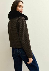 Bruine geblokte cropped jack met een zwart faux fur kraag, met een gestructureerde vorm en zichtbare naden. Draagt met donkere spijkerbroeken.