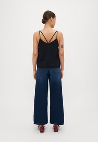 Svart spaghetti-axel topp med lös passform, kombinerad med vida mörka denimjeans. Anmärkningsvärda detaljer inkluderar en baksidesdesign med korsade axelband.