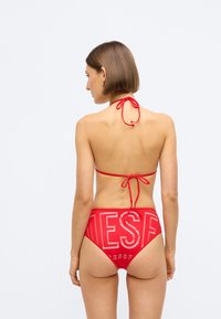 Κόκκινο μπικίνι σετ με λαιμόκοψη halter και ψηλόμεσο κάτω μέρος με μεγάλα λευκά γράμματα στο πίσω μέρος. Λείο ύφασμα και ρυθμιζόμενοι κορδόνες.
