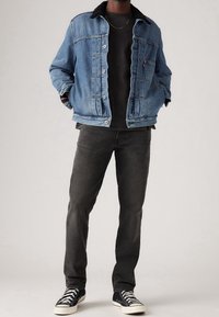 Jeansjacka i ljusblått med sherpa-krage, bärs över en svart t-shirt, kombinerad med mörkgrå byxor och svarta sneakers.