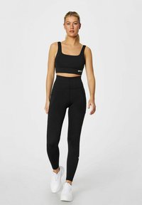 Svart crop top og høyt liv leggings-sett, laget av elastisk stoff. Har en tettsittende design og logo aksent på båndet.