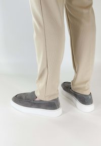 Grijze suède instappers met witte rubberen zolen, zichtbare naden en een minimalistisch ontwerp, gecombineerd met beige getextureerde broeken.