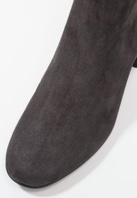 Szare zamszowe botki za kostkę z eleganckim, spiczastym noskiem i niskim obcasem. Powierzchnia ma miękką teksturę, co podkreśla ich minimalistyczny design.