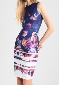 Robe sans manches avec un motif floral bleu marine, présentant des fleurs multicolores et un ourlet blanc avec des bandes florales horizontales.