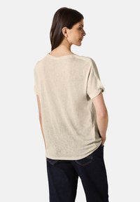 Ljusbeige kortärmad T-shirt med en avslappnad passform, uppvikta ärmar och diskret textur. Har en rund halsringning och enkel design.