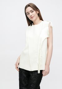 Valge varrukateta top, millel on vasakul õlal tekstuuriga lõheroheline detail, ümara kaelusega ja sirge lõikega. Mustad tekstuuriga püksid.