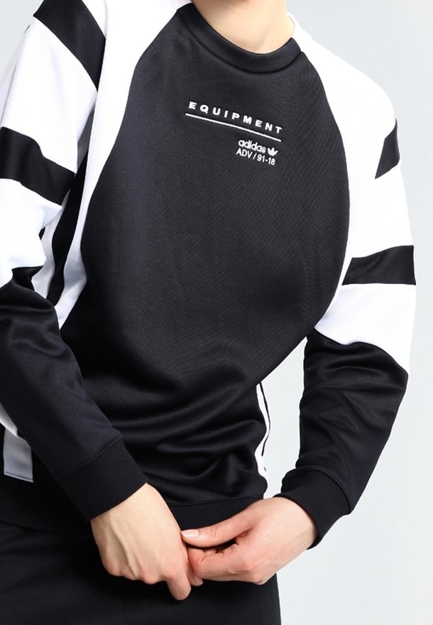 Svart och vit sweatshirt med rund nacke, med geometriska vita ränder på ärmarna, texturerat tyg och "EQUIPMENT"-logotyp på bröstet.