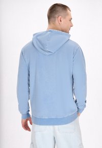 Felpa con cappuccio di colore azzurro chiaro, in tessuto morbido, vestibilità comoda, polsini e orlo a costine, con un design semplice e senza loghi o grafiche visibili.