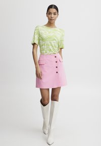 Groen en wit geblokte shirt gecombineerd met een roze A-lijn rok met bruine knopen en zakken; het model draagt witte kniehoogte laarzen.