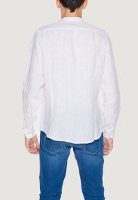 Camicia bianca in lino a maniche lunghe con orlo curvo, polsi con bottoni e colletto classico; abbinata a jeans in denim blu.