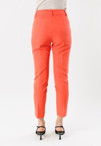Pantaloni coral su misura con vestibilità slim, vita media, davanti piatto e tasche laterali. Gambe affusolate con orlo cropped e tacchi neri eleganti.