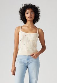 Lys beige strikket tanktop med kabelmønstre og flerfarvede broderede stjerner. Har tynde justerbare stropper og en ribbet kant.