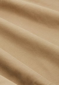 Béžová látka s hladkým povrchem, uspořádaná v jemných záhybech, vykazuje mírně lesklý povrch a konzistentní barvu po celém povrchu.
