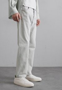 Jeans dritti grigi chiari con una texture liscia, design a cinque tasche, abbinati a sneaker bianche. Aspetto semplice e moderno.