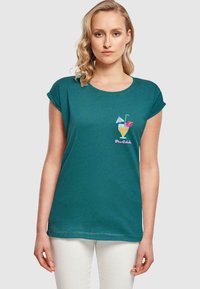 Türkises T-Shirt mit kurzen Ärmeln, das eine bunte Cocktailillustration mit einem Strohhalm und dekorativen Elementen zeigt. Weicher Stoff mit lockerem Schnitt.