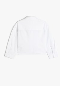 Camisa blanca corta con mangas largas, cuello puntiagudo, puños abotonados y una textura suave; presenta un diseño limpio y sencillo.
