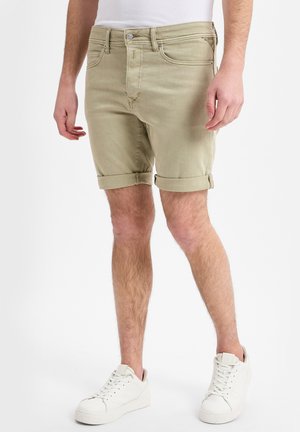 Beige denimshorts med uppvikta kanter, fem fickor och knäppning fram, som har parats ihop med vita sneakers. Slät textur.