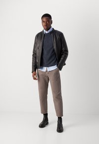 Veste en cuir noire, pull côtelé bleu marine, chemise bleu clair, pantalon beige et bottines noires. Textures lisses et design ajusté.