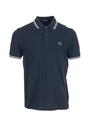 Polo azul marino de manga corta con doble raya blanca en el cuello y los puños, dos botones y un pequeño logo de corona de laurel en el pecho.
