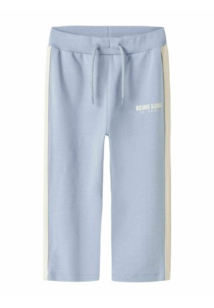 Pantalon de survêtement bleu clair avec des bandes blanches sur les côtés et une taille à cordon, avec le texte "BEING KIND IS COOL" sur la cuisse gauche.