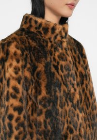 Manteau en fausse fourrure imprimé léopard avec un col haut, présentant une texture douce dans des tons chauds de marron et de noir, mettant en avant un motif audacieux.