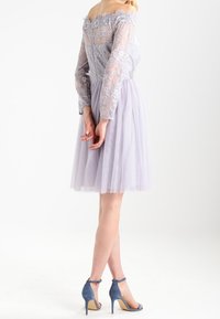Krajková šaty bez ramínek v jemné levandulové barvě s dlouhými rukávy a sukní z tylu. Doplněné modrými sandály na podpatku s kotníkovými řemínky.