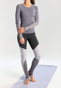 Grå langærmet top med en tætsiddende design og lysegrå accenter, parret med farveblokerede leggings i mørkegrå, lysegrå og mellemgrå.