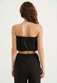 Top corto nero senza spalline con texture arricciata e orlo elastico, abbinato a pantaloni a vita alta con una texture simile.