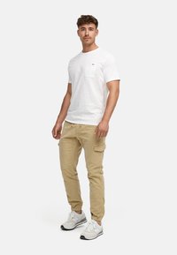 Camiseta blanca de manga corta con un bolsillo en el pecho, combinada con pantalones cargo beiges y zapatillas blancas con acentos en gris y negro.