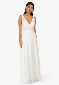 Weißes Maxikleid mit tiefem V-Ausschnitt, Spitzenverzierungen am Oberteil und fließendem Rock; hat dünne Träger und eine glatte Textur.